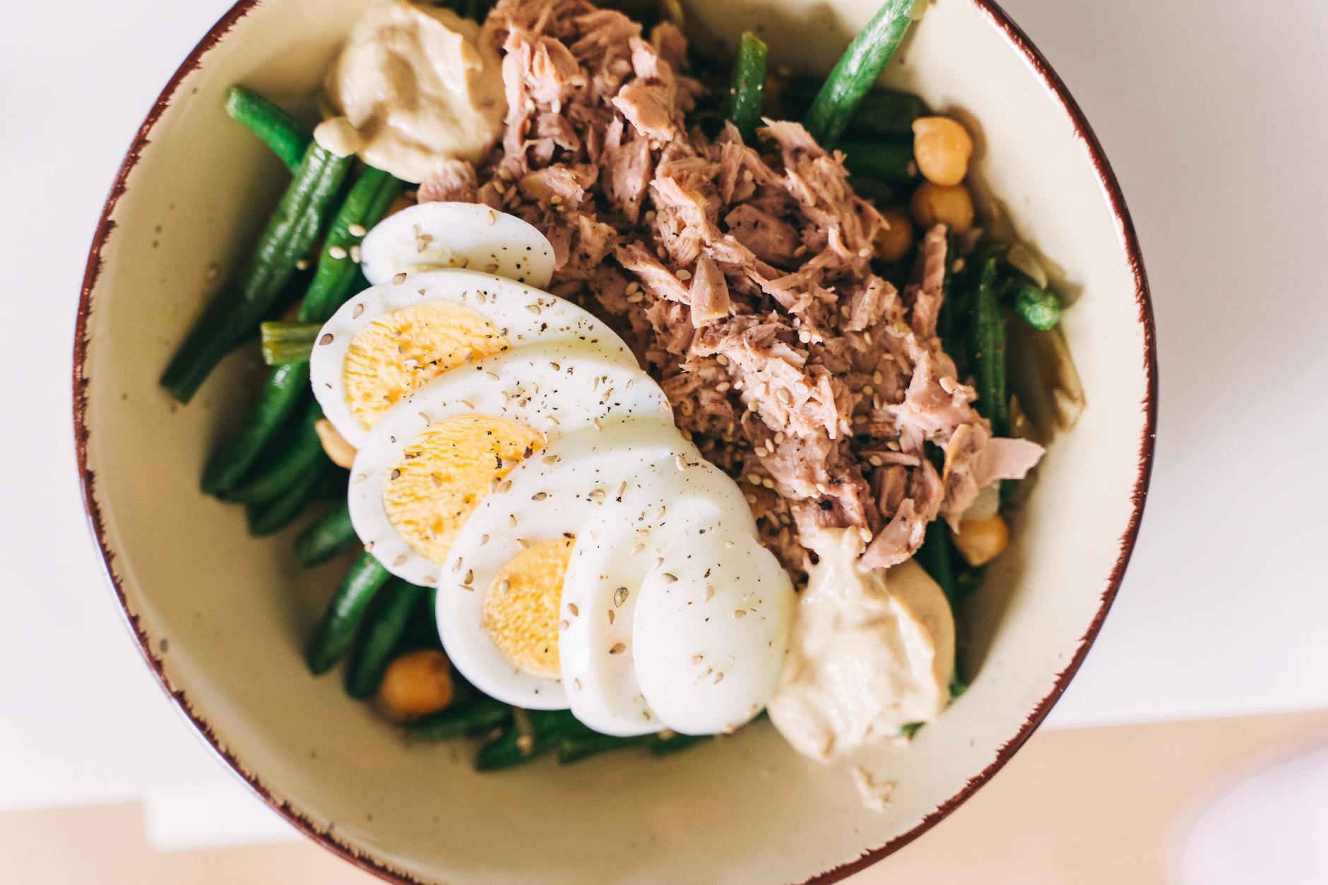Bowl with sliced boiled eggs, flaked tuna, green beans, chickpeas and hummus