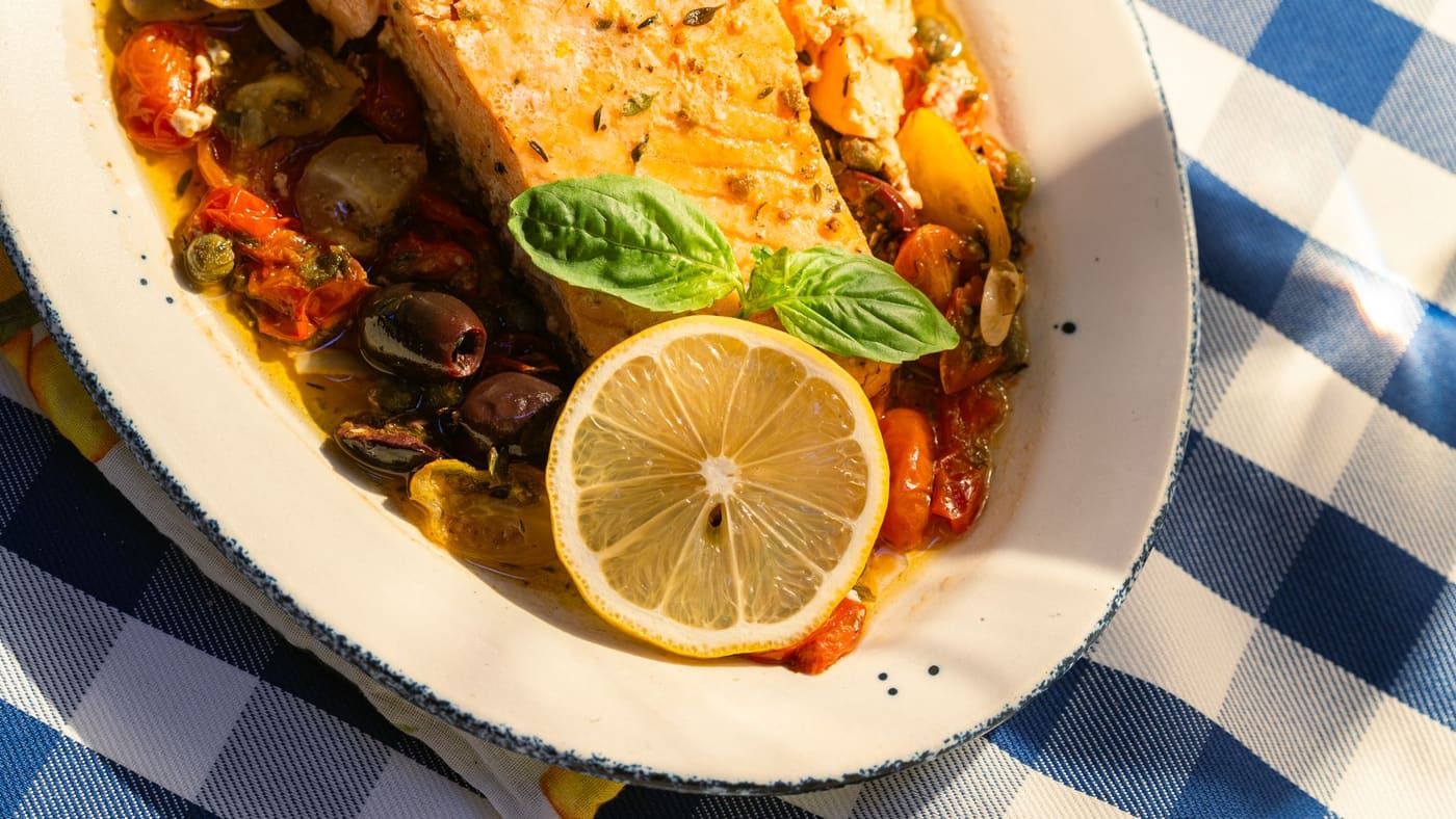 Grilled salmon topped with lemon slices and basil on a sunlit table