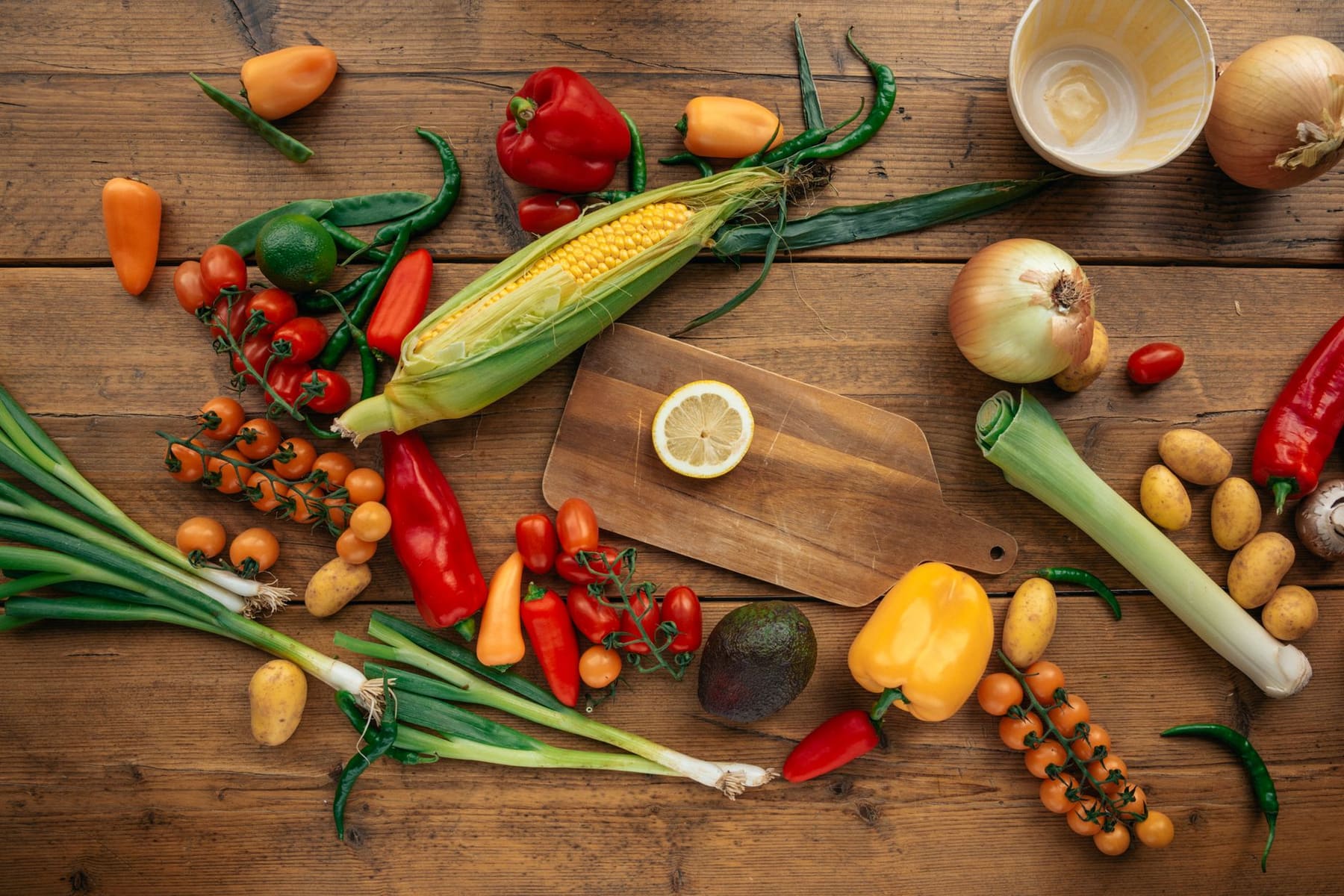 Flat lay of colorful fresh vegetables, peppers, corn and herbs on a dark wooden table