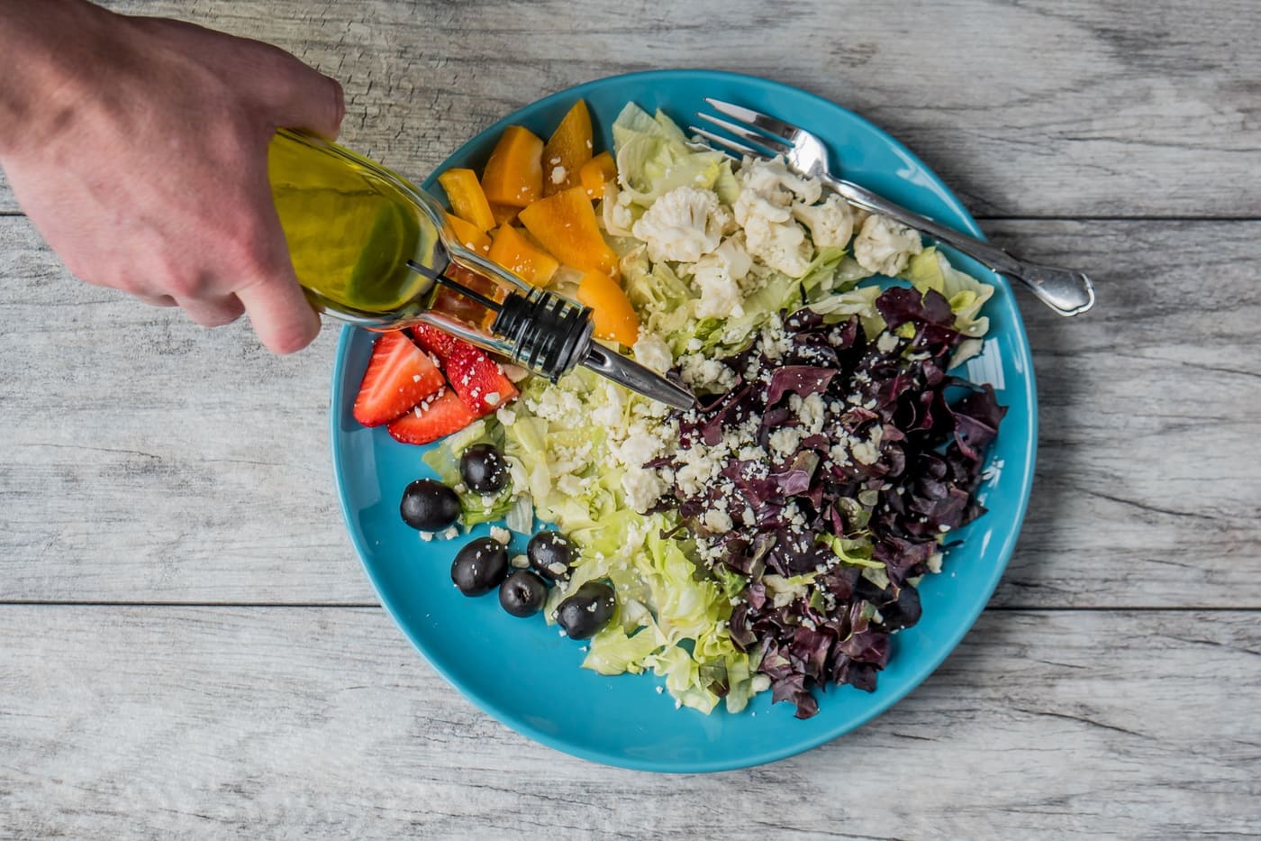 Olive oil being drizzled over a plate of salad with olives, orange slices and strawberries