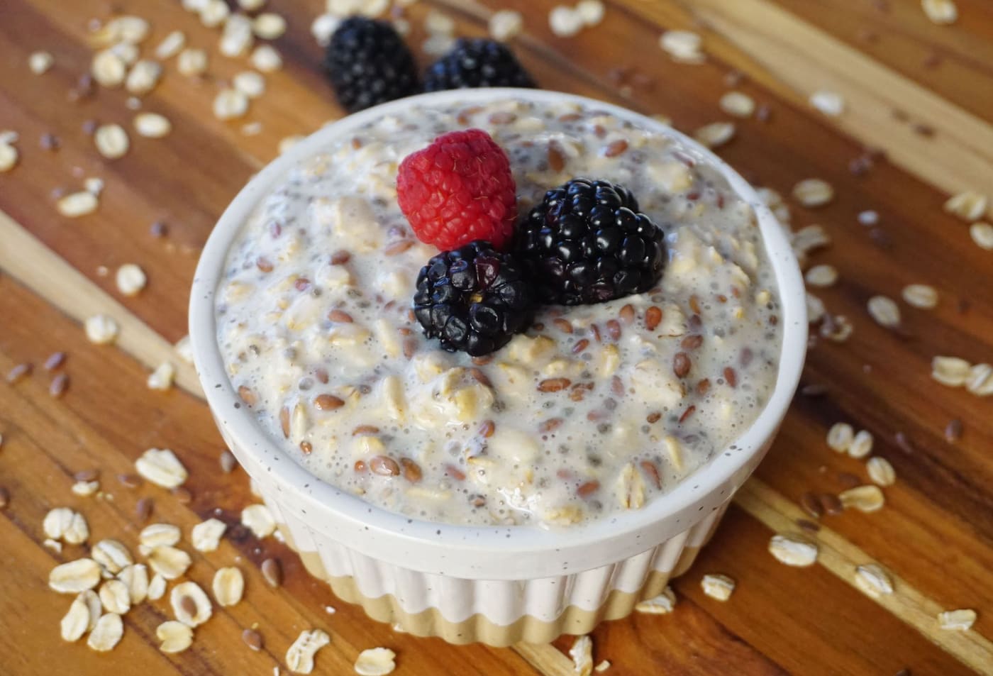 A jar of overnight oats topped with raspberries and blackberries on a wooden board scattered with oats